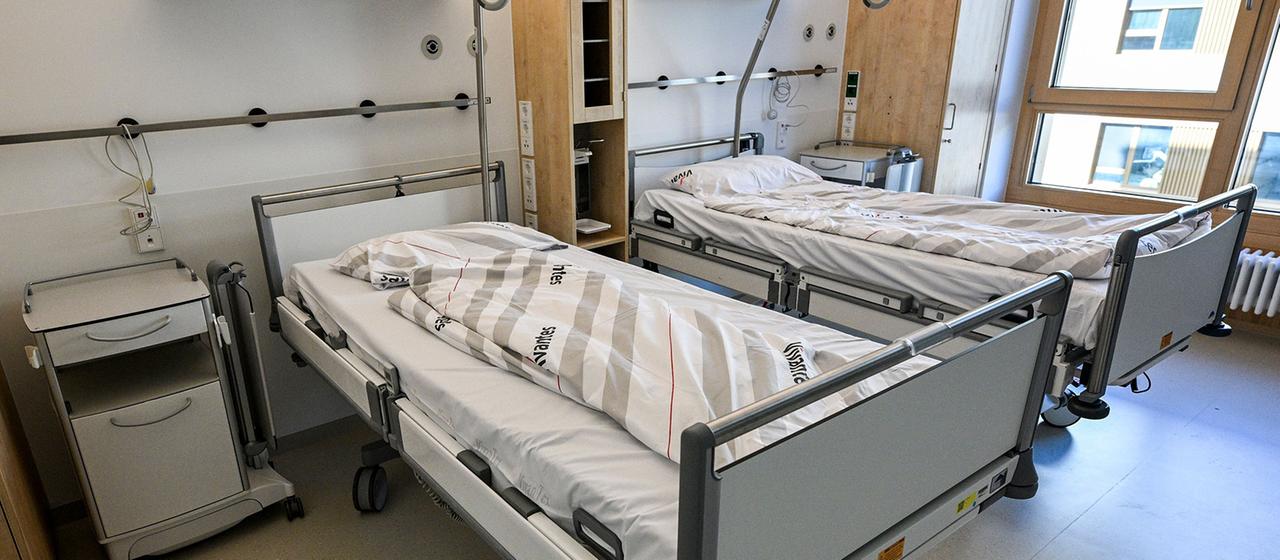 Betten stehen in einem Krankenhauszimmer.