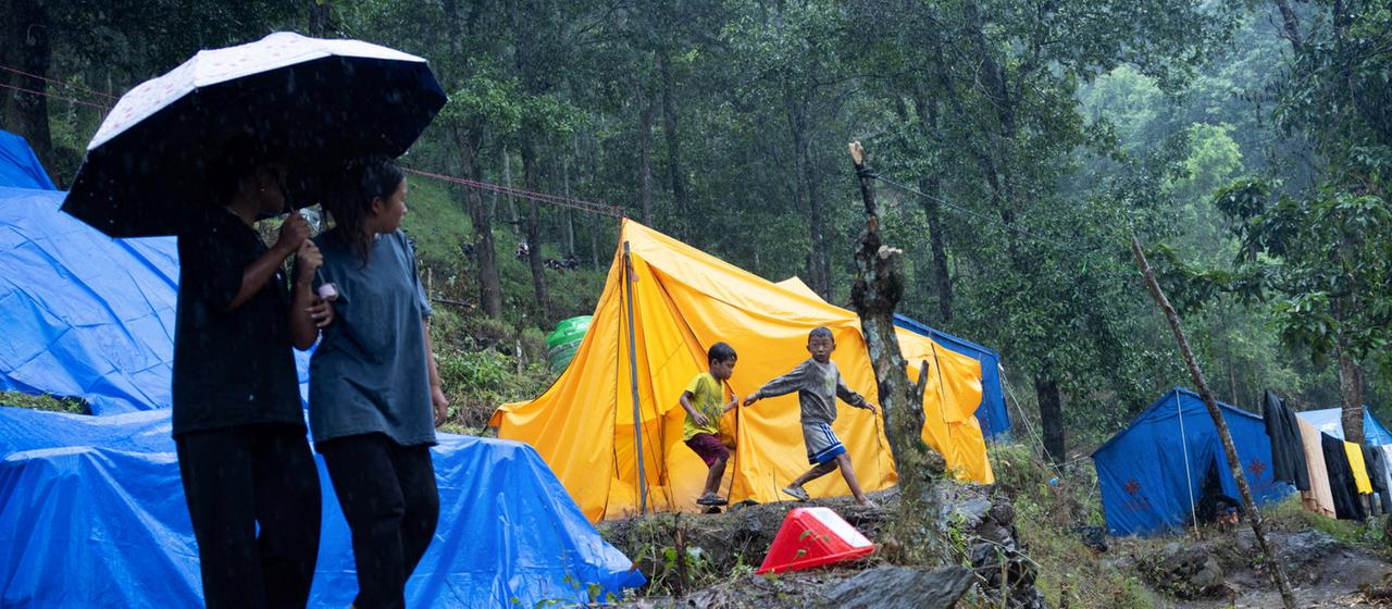 Menschen stehen im Regen vor Zelten in Betrawati, Nepal.