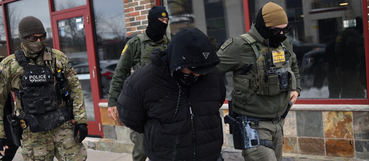 ICE-Beamte führen einen Mann ab.