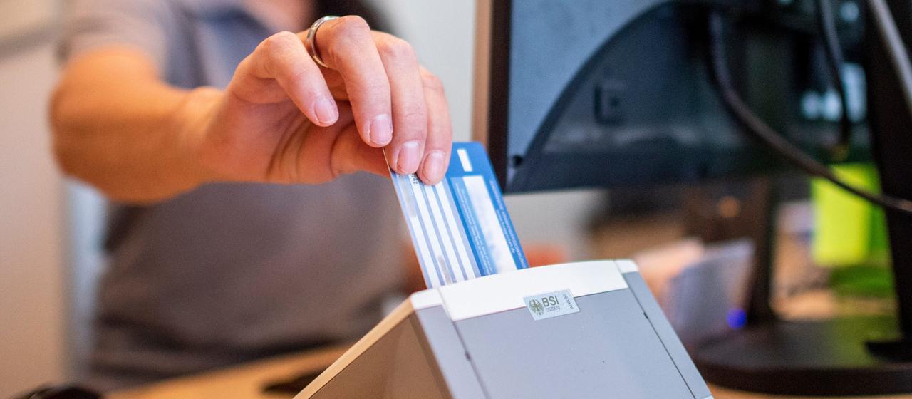 Eine Person schiebt eine Versichertenkarte einer Krankenkasse in eine Lesegerät. 