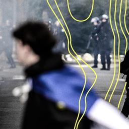 Junge Menschen stehen in einer raucherfüllten Straße und blicken auf die in der Ferne positionierte Polizei.