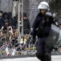 Ein griechischer Bereitschaftspolizist patrouilliert an der Grenze zur Türkei, während Migranten hinter einem Stacheldrahtzaun warten.