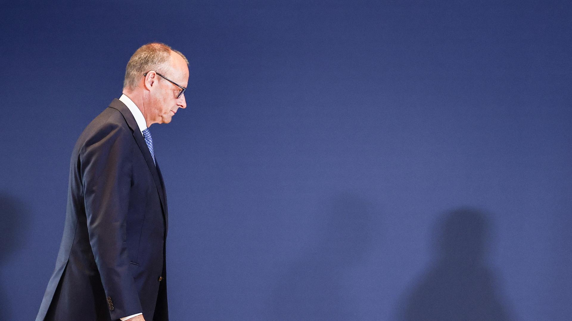 Friedrich Merz geht vor einer blauen Wand entlang. | EPA