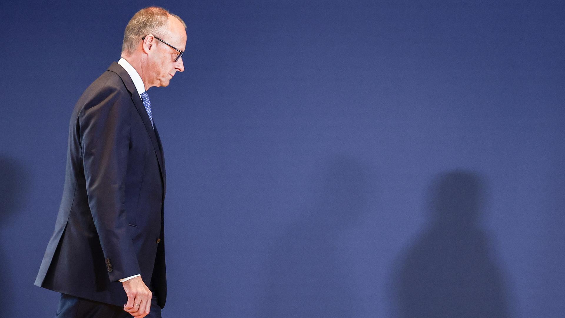Friedrich Merz geht vor einer blauen Wand entlang. | EPA