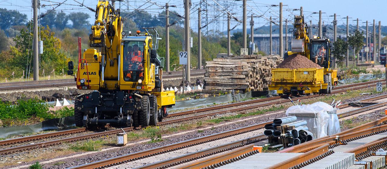Gleisbaufahrzeuge rollen nahe des Bahnhofs Schönhausen an Gleisbauteilen vorbei.