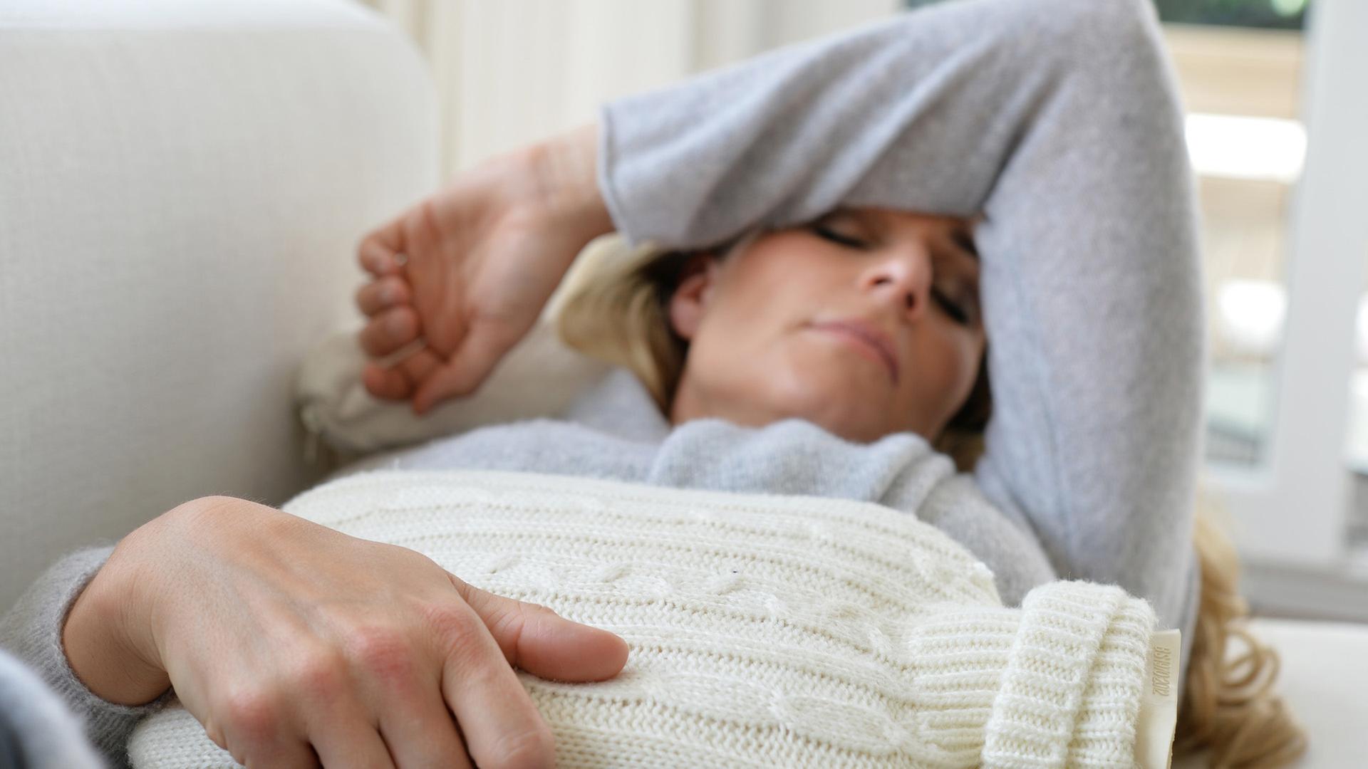 Eine Frau liegt mit einer Wärmflasche auf dem Sofa. | picture alliance / Frank May