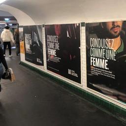 Menschen gehen an einer Plakatwand in einer Metro-Unterführung in Paris vorbei, darauf steht "Fahre Auto wie eine Frau" ("Conduisez comme une femme").