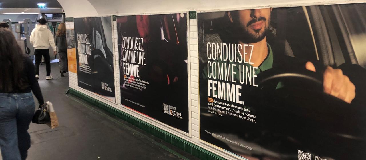 Menschen gehen an einer Plakatwand in einer Metro-Unterführung in Paris vorbei, darauf steht "Fahre Auto wie eine Frau" ("Conduisez comme une femme").