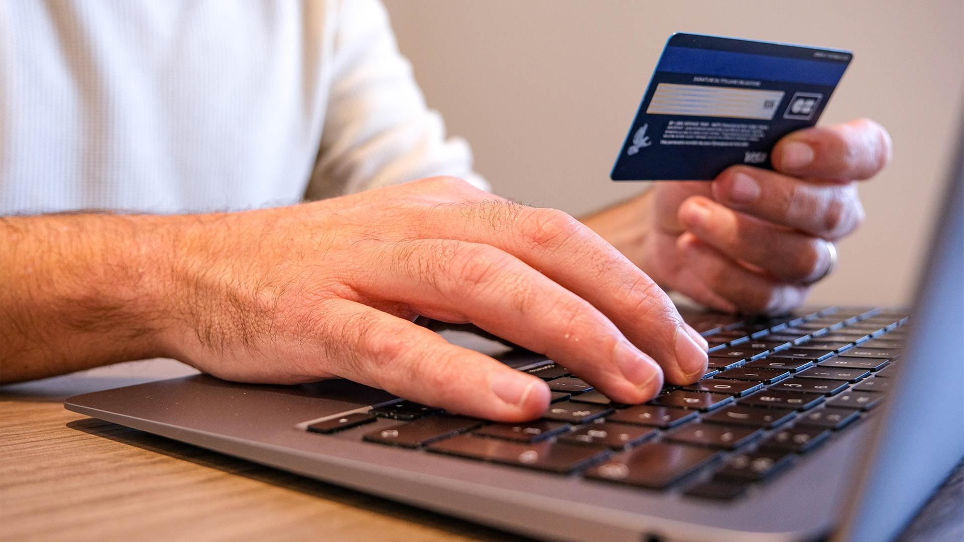 Ein Mann sitzt mit Kreditkarte an einem Laptop und gibt Daten ein. | picture alliance / Hans Lucas