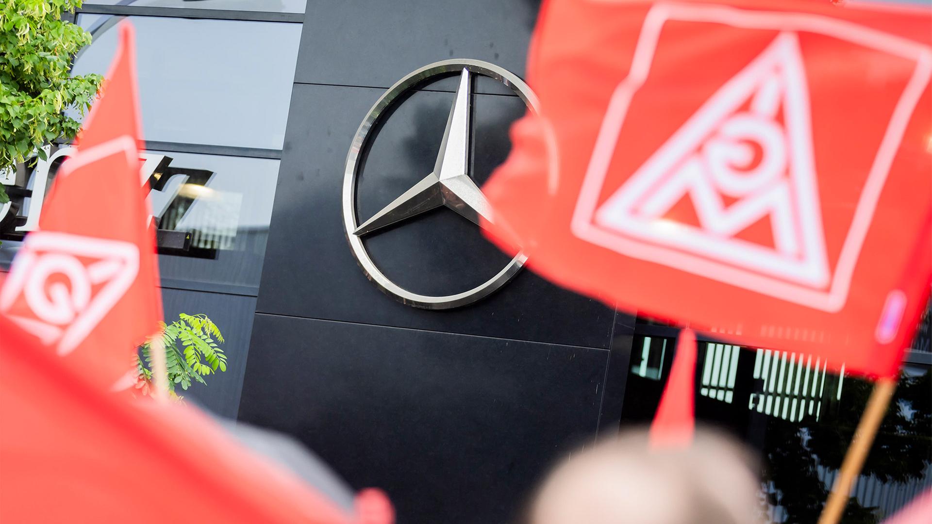 Flaggen der IG-Metall bei einer Kundgebung. Im Hintergrund ein Mercedes-Stern. | picture alliance/dpa