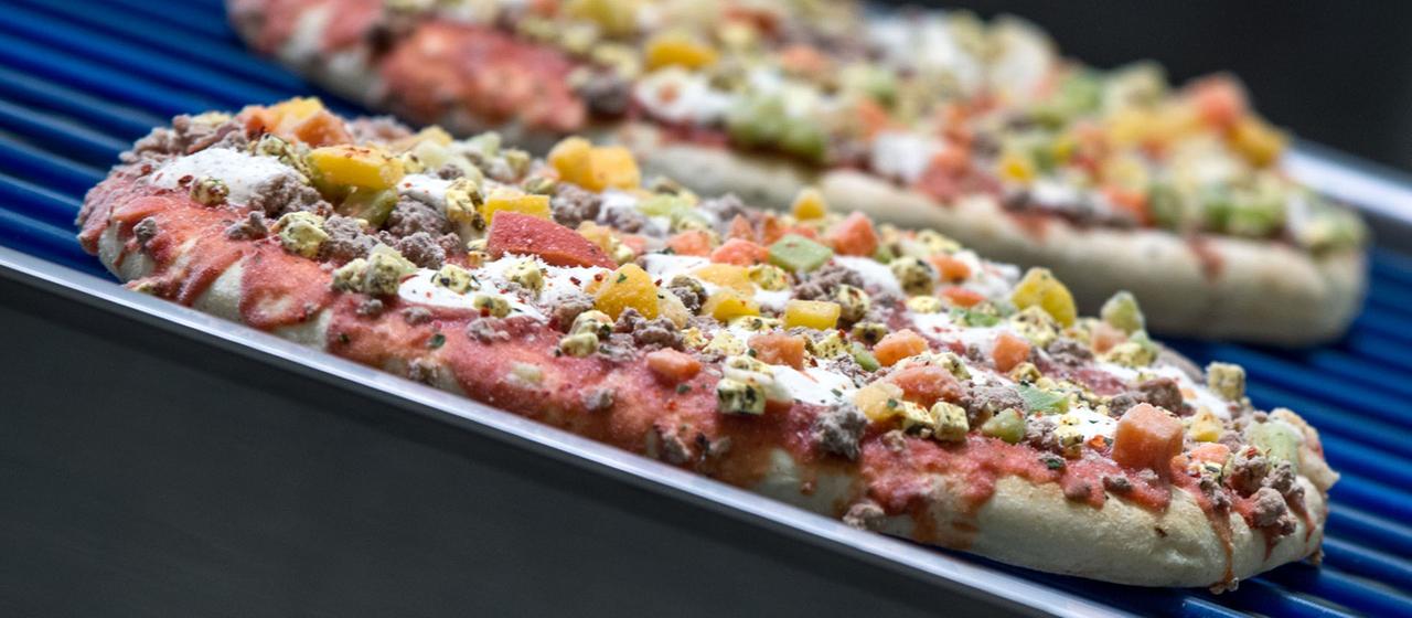 Tiefgefrorene Pizzen laufen über ein Transportband. 