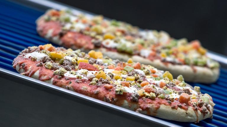 Tiefgefrorene Pizzen laufen über ein Transportband. 