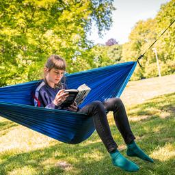 Eine junge Frau in einer Hängematte liest in einem Buch. 