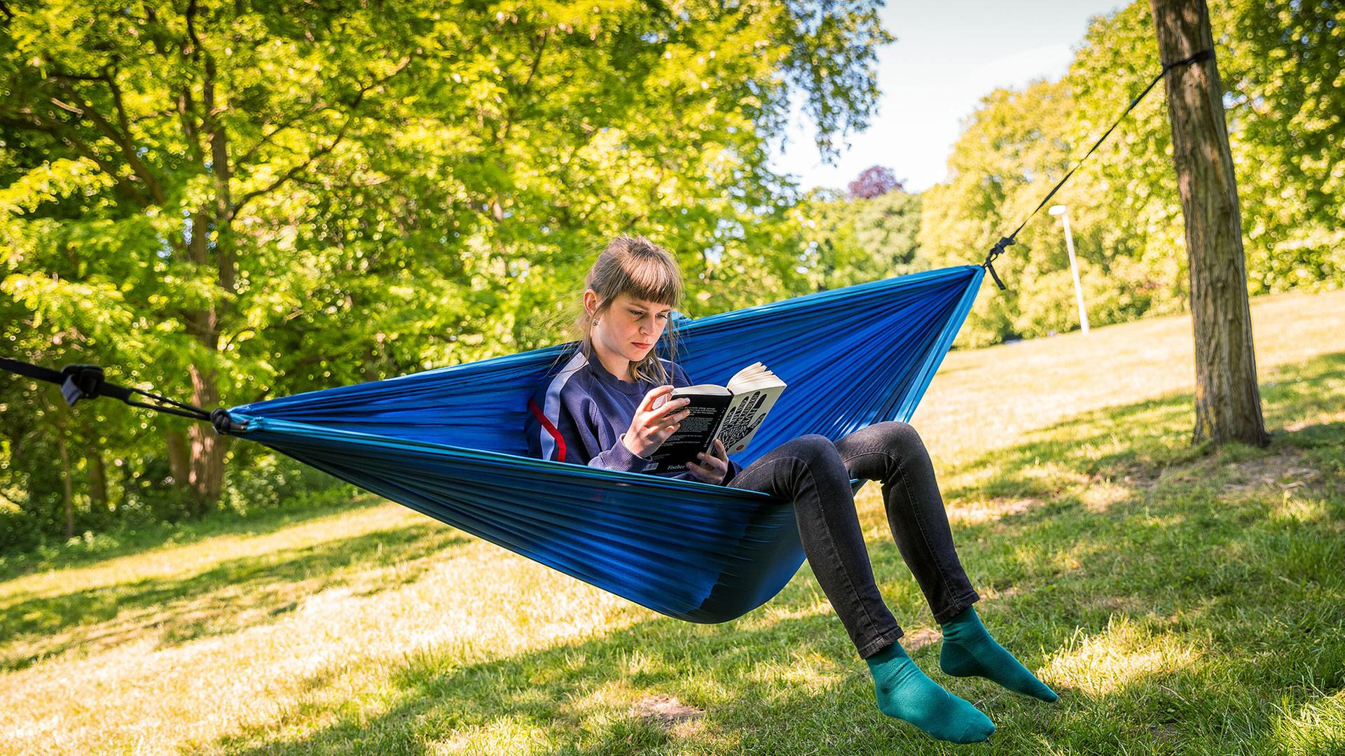 Eine junge Frau in einer Hängematte liest in einem Buch.  | picture alliance/dpa