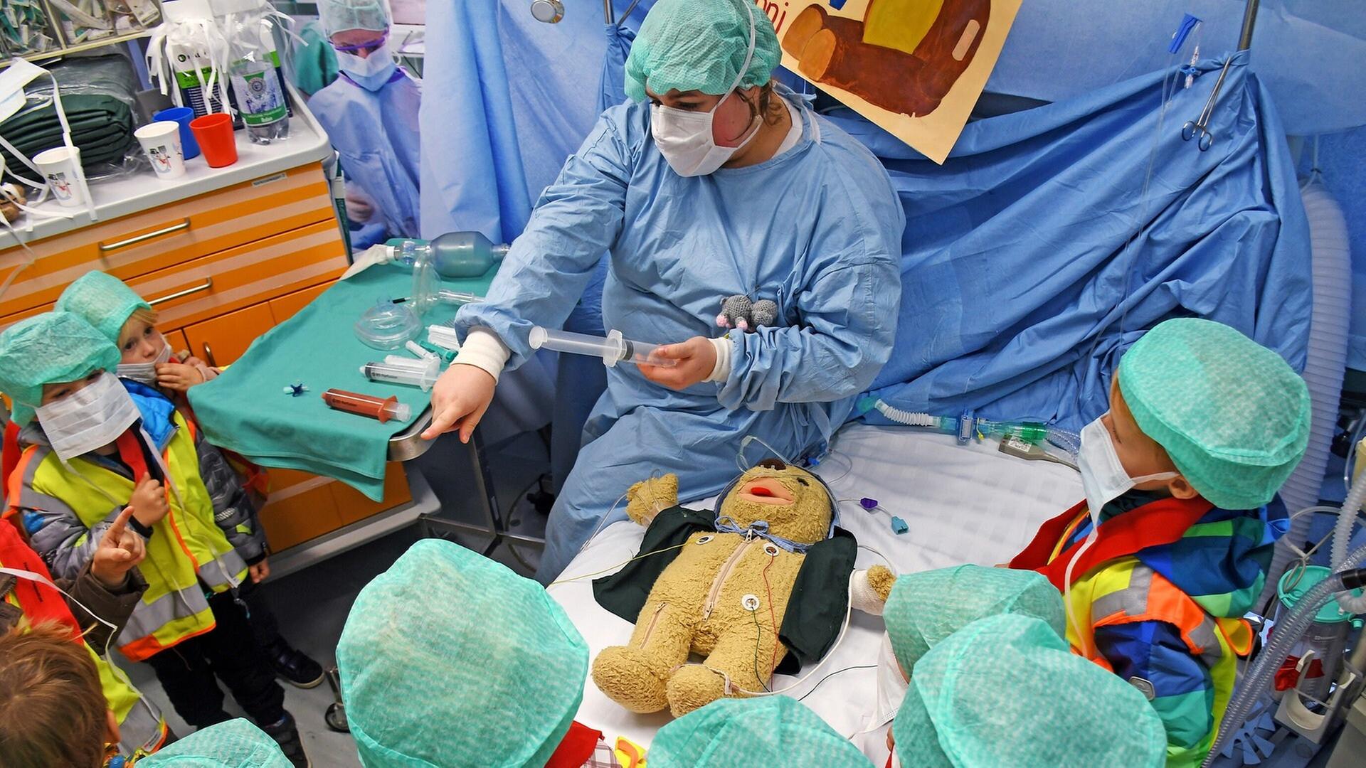 Ein Arzt in Kittel und Kinder sitzen um einen OP-Tisch mit einem Teddybären darauf. Die Teddyklinik der Mainzer Universitätsmedizin wird 25 Jahre alt | dpa Bildfunk, Picture Alliance