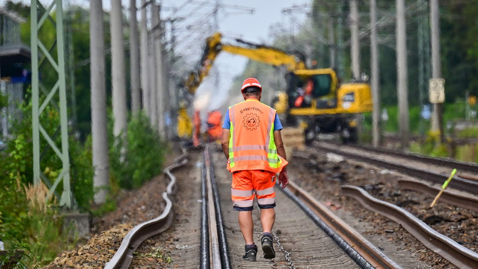 Ein Arbeiter geht auf Bahngleisen in Richtung eines Baggers. | picture alliance/dpa