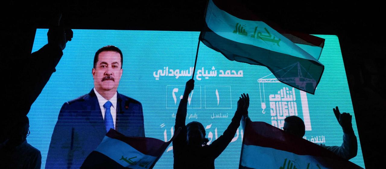Anhänger des amtierenden irakischen Premierministers Mohammed Shia al-Sudani schwenken Nationalflaggen vor einem Bildschirm, auf dem sein Porträt zu sehen ist