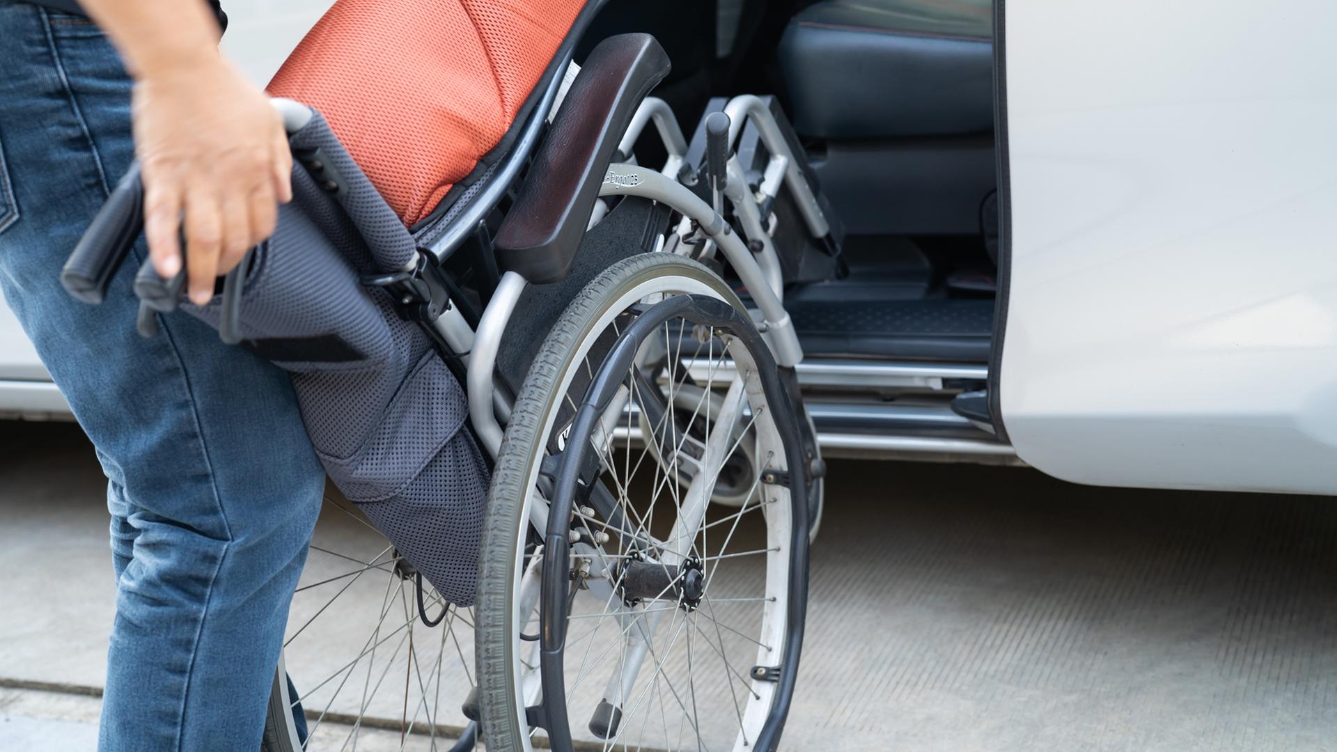 Eine Frau stellt einen Rollstuhl in ein Auto. | IMAGO/Panthermedia