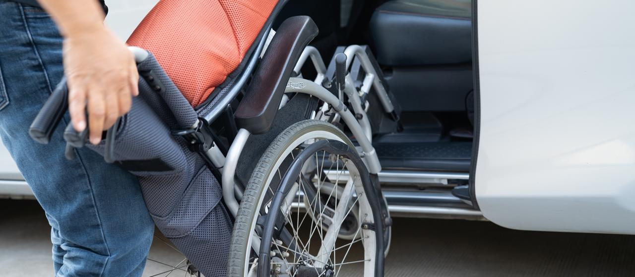 Eine Frau stellt einen Rollstuhl in ein Auto.
