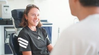 Sophia Schneider sitzt bei ihrem Zahnarzt Siegfried Marquardt auf dem Behandlungsstuhl und lächelt.