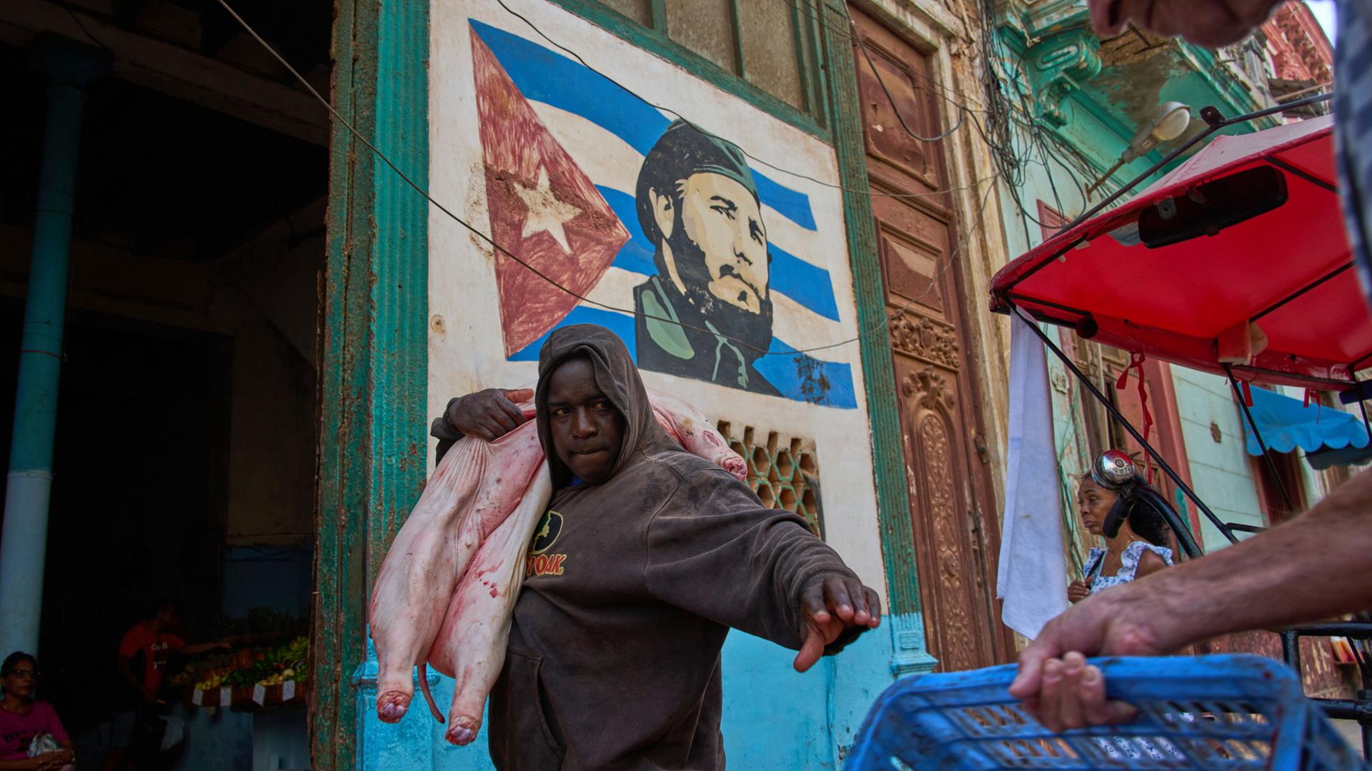 Ein Mann auf dem Weg zum Markt, im Hintergrund hängt ein Bild von Fidel Castro in Havanna. | AP Photo/Ramon Espinosa