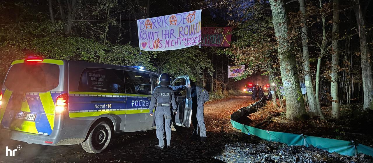Polizeibeamte stehen neben einem Einsatzfahrzeug am Eingang eines Protestcamps im Langener Wald.