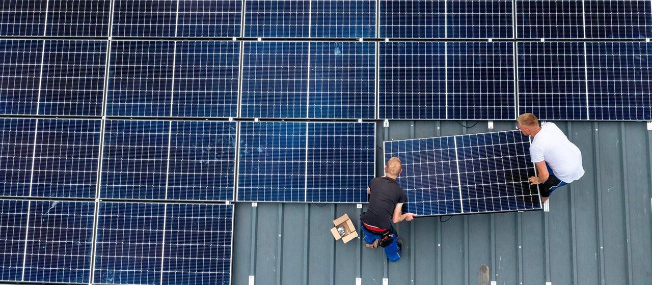 Zwei Arbeiter bei der Montage von Solarmodulen auf das Dach einer Scheune.