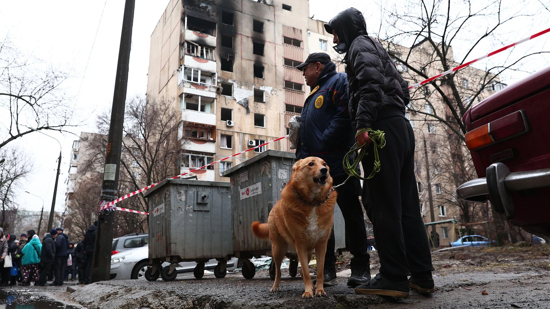 Anwohner stehen in der Nähe eines zerstörten Wohnhauses in Saporischschja. | Kateryna Klochko/AP/dpa