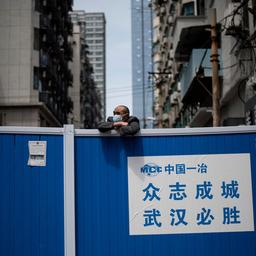 Ein Mann mit einer Gesichtsmaske blickt über eine Barrikade, die errichtet wurde, um Menschen aus einem Wohngebiet in Wuhan in der zentralchinesischen Provinz Hubei fernzuhalten (Archiv).