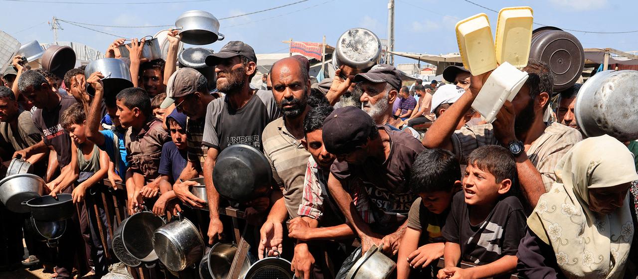 Palästinenser halten Töpfe und Behälter in den Händen, während sie darauf warten, Lebensmittel aus einer Suppenküche im südlichen Gazastreifen zu erhalten. | REUTERS Palästinenser halten Töpfe und Behälter in den Händen, während sie darauf warten, Lebensmittel aus einer Suppenküche im südlichen Gazastreifen zu erhalten.