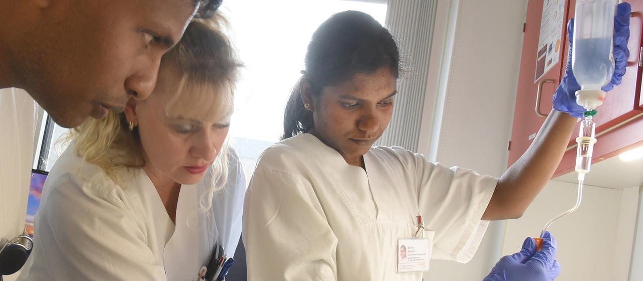 Eine Praxisanleiterin erklärt  angehenden indischen Pflegefachkräften das Vorbereiten einer Infusion.
