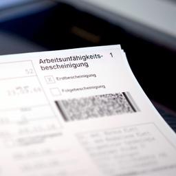 Eine Arbeitsunfähigkeitsbescheinigung liegt auf dem Drucker in einer Arztpraxis.