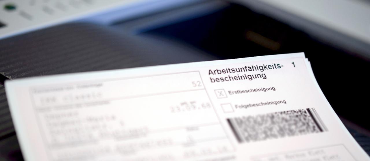 Eine Arbeitsunfähigkeitsbescheinigung liegt auf dem Drucker in einer Arztpraxis.