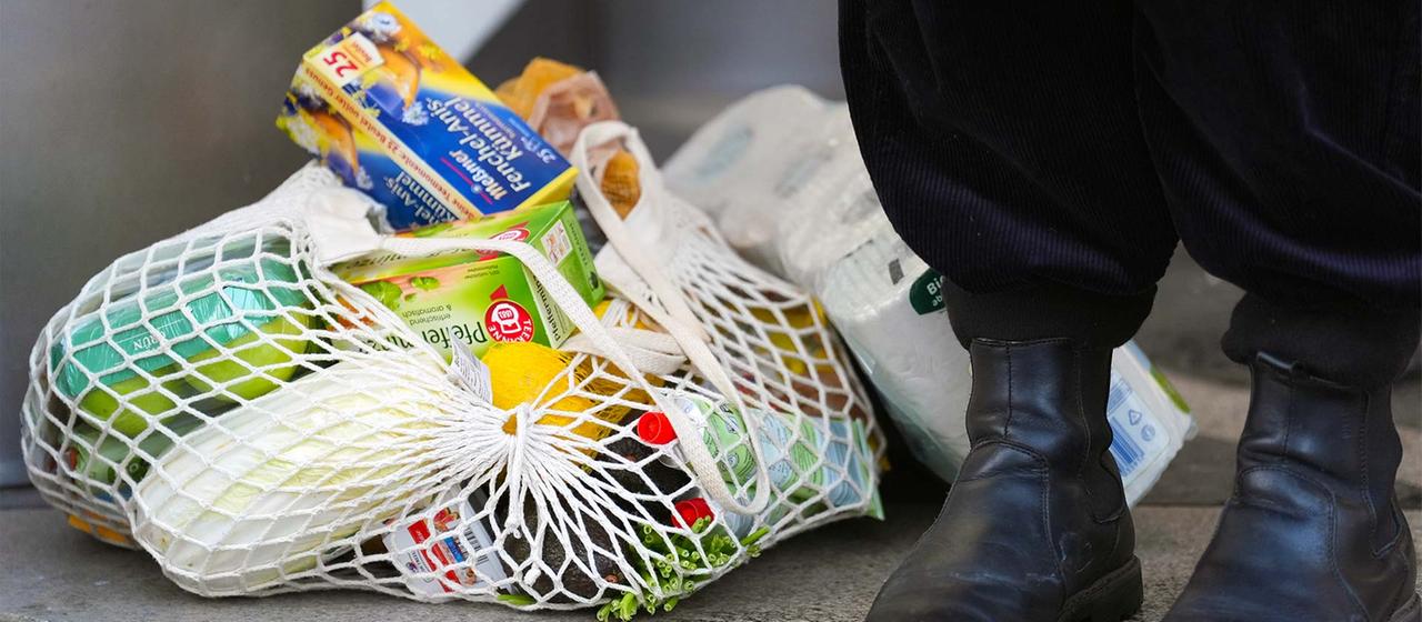 Eine Person steht neben ihren Einkäufen vor einem Supermarkt.