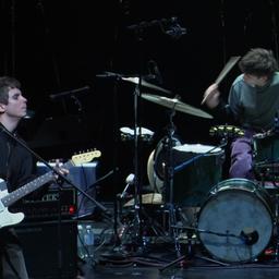 Ein Mann mit E-Gitarre und ein Schlagzeuger musizieren auf einer Bühne