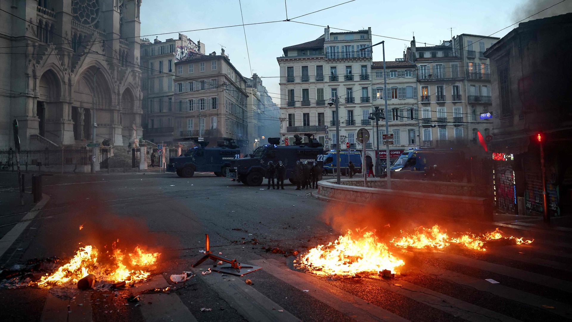 Auf einer Straße in Marseille sind Flammen vor gepanzerten Polizeifahrzeugen zu sehen. | AFP