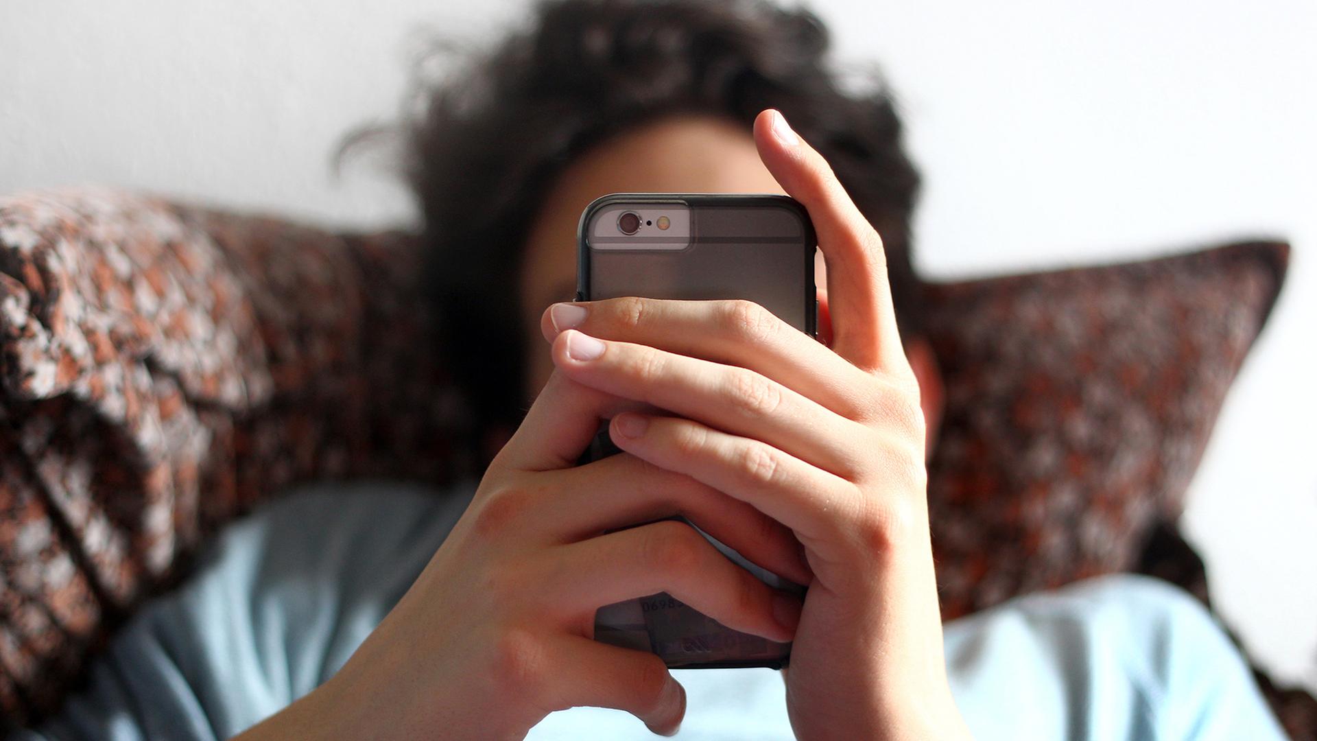 Ein Jugendlicher hält ein Handy in den Händen. | dpa