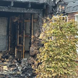 Verkohlte Balken eines Gebäudes. Davor ein Busch mit Herbstlaub