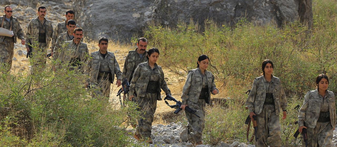 Mehrere Mitglieder der PKK laufen mit Gewehren durch eine steinige, buschige Landschaft im Nordirak. | REUTERS Mehrere Mitglieder der PKK laufen mit Gewehren durch eine steinige, buschige Landschaft im Nordirak.