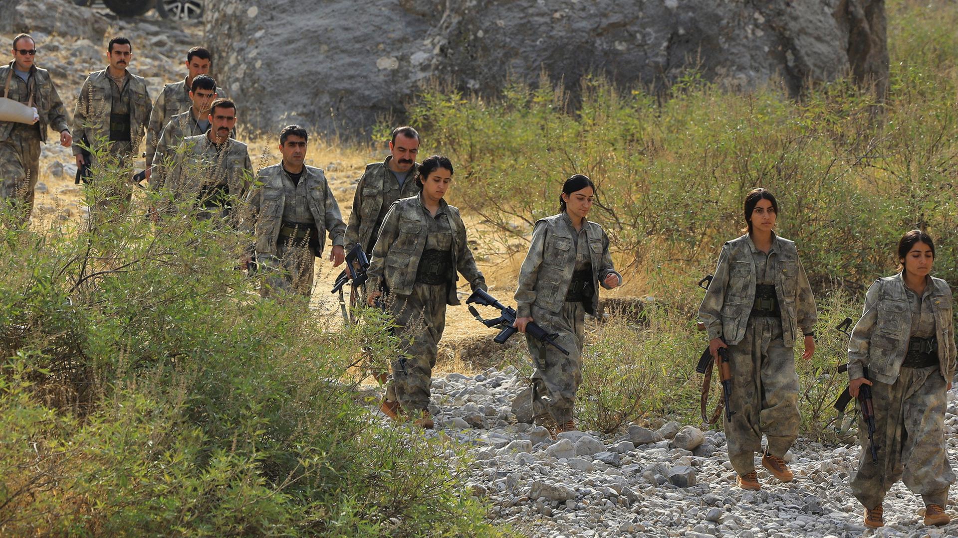 Mehrere Mitglieder der PKK laufen mit Gewehren durch eine steinige, buschige Landschaft im Nordirak. | REUTERS