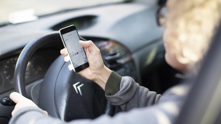 Eine Autofahrerin hält während der Fahrt ein Smartphone in der Hand.