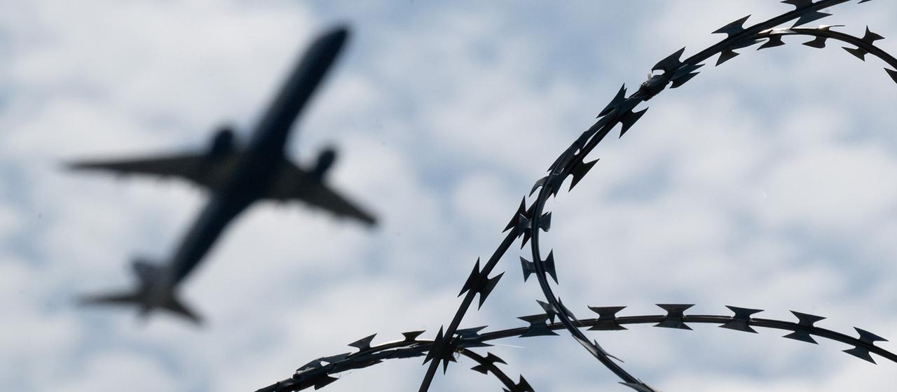 Ein Flugzeug hebt hinter einem Zaun mit Natodraht ab.