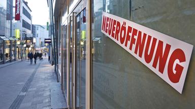 Neueröffnung-Schild in einem Schaufenster in einer Fußgängerzone.