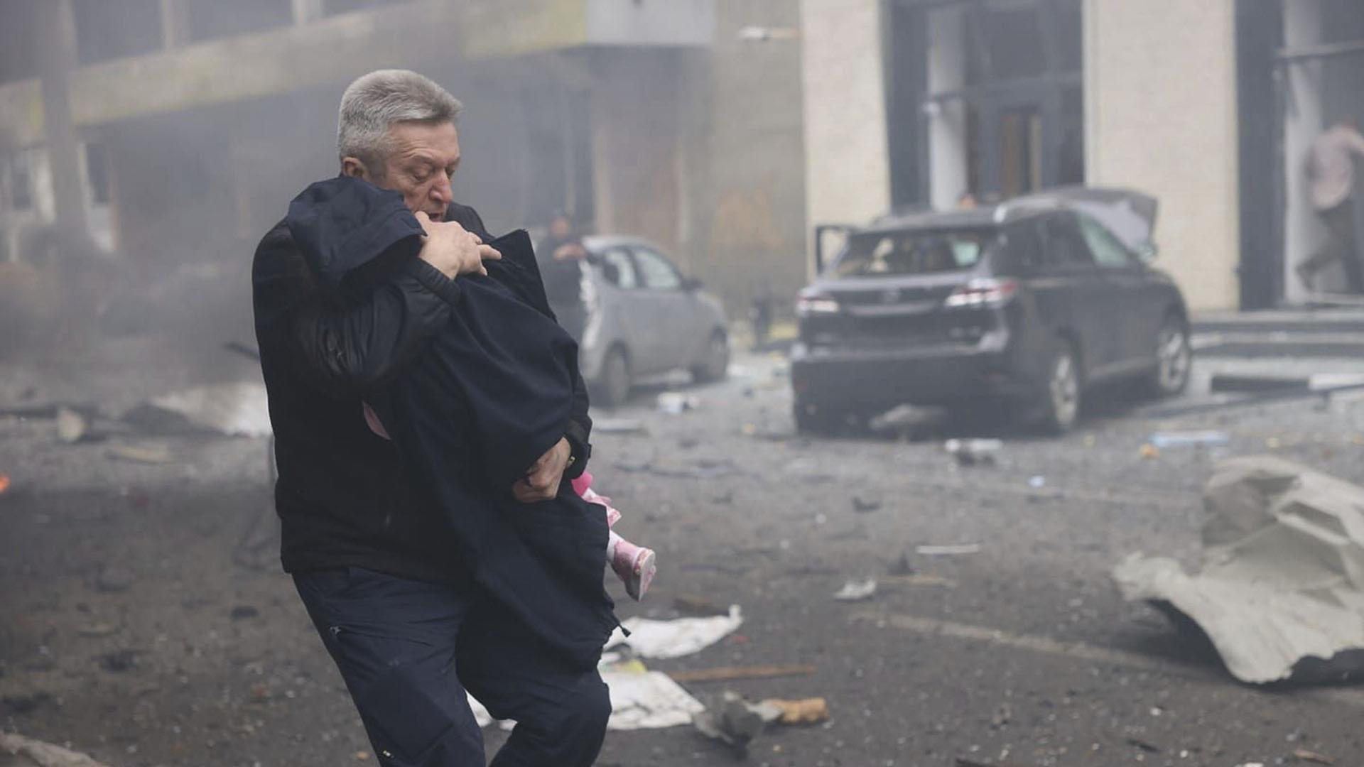Ein Mann evakuiert ein Kind aus einem Kindergarten in Charkiw. | Uncredited/Ukrainian Emergency Service via AP/dpa