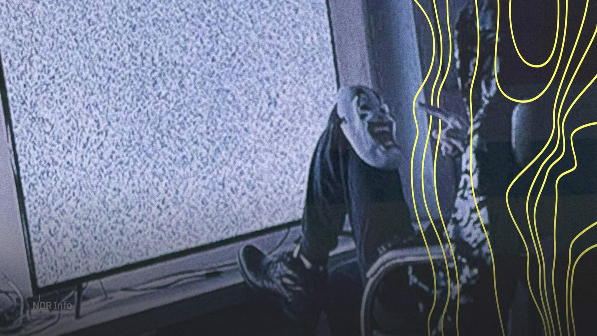 Ein Mann mit Maske sitzt auf einem Stuhl vor einem Fernseher. Auf seinem Knie liegt eine Maske mit Grimasse. | Polizei Hamburg