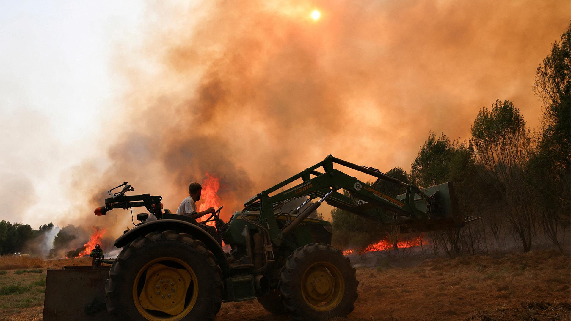 Ein Mann fährt auf einem Traktor vor lodernden Brandherden. | REUTERS