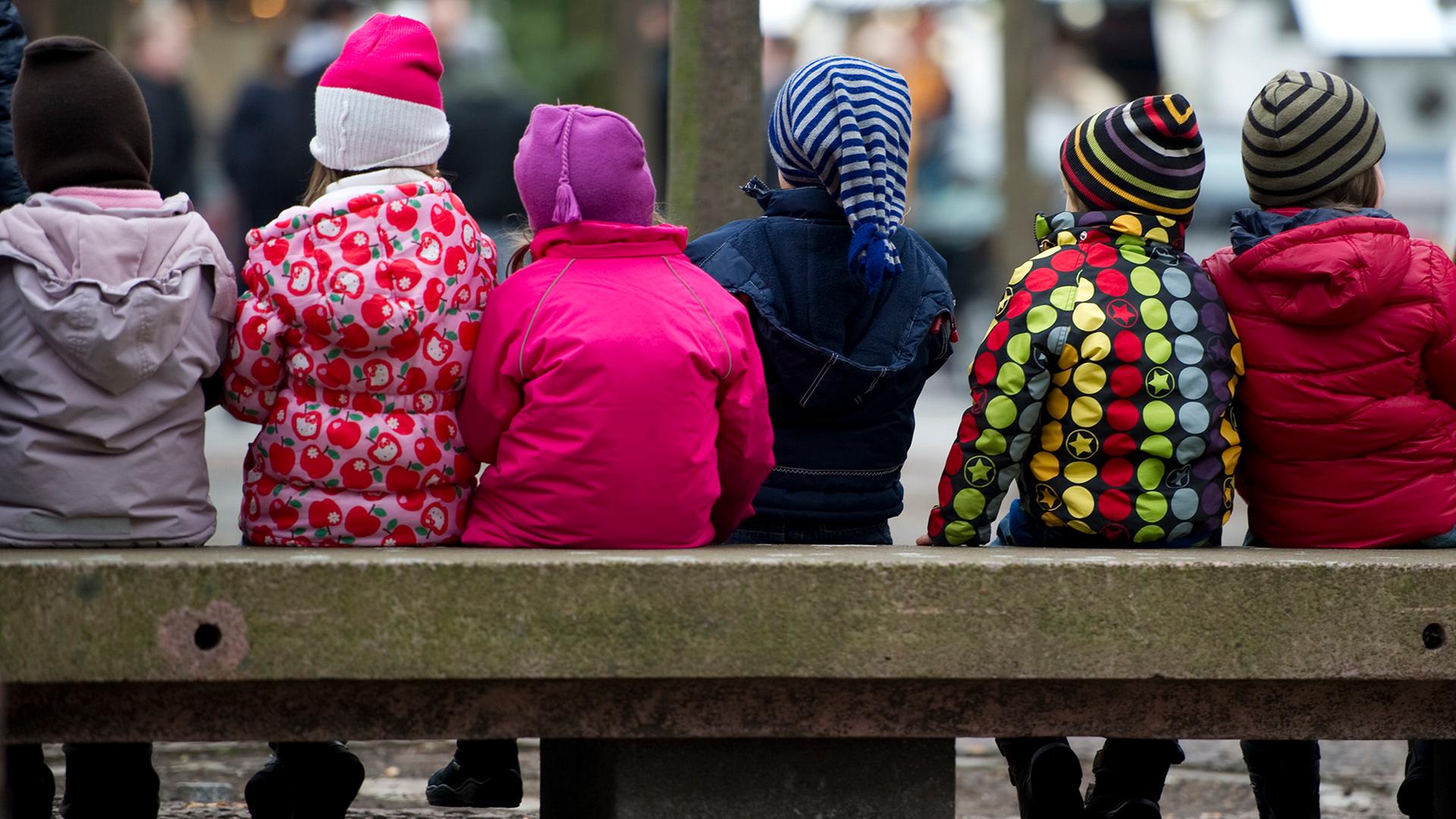 Kinder in Jacken und Mützen sitzen auf einer Bank. | picture alliance / Zentralbild