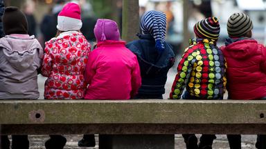 Kinder in Jacken und Mützen sitzen auf einer Bank.