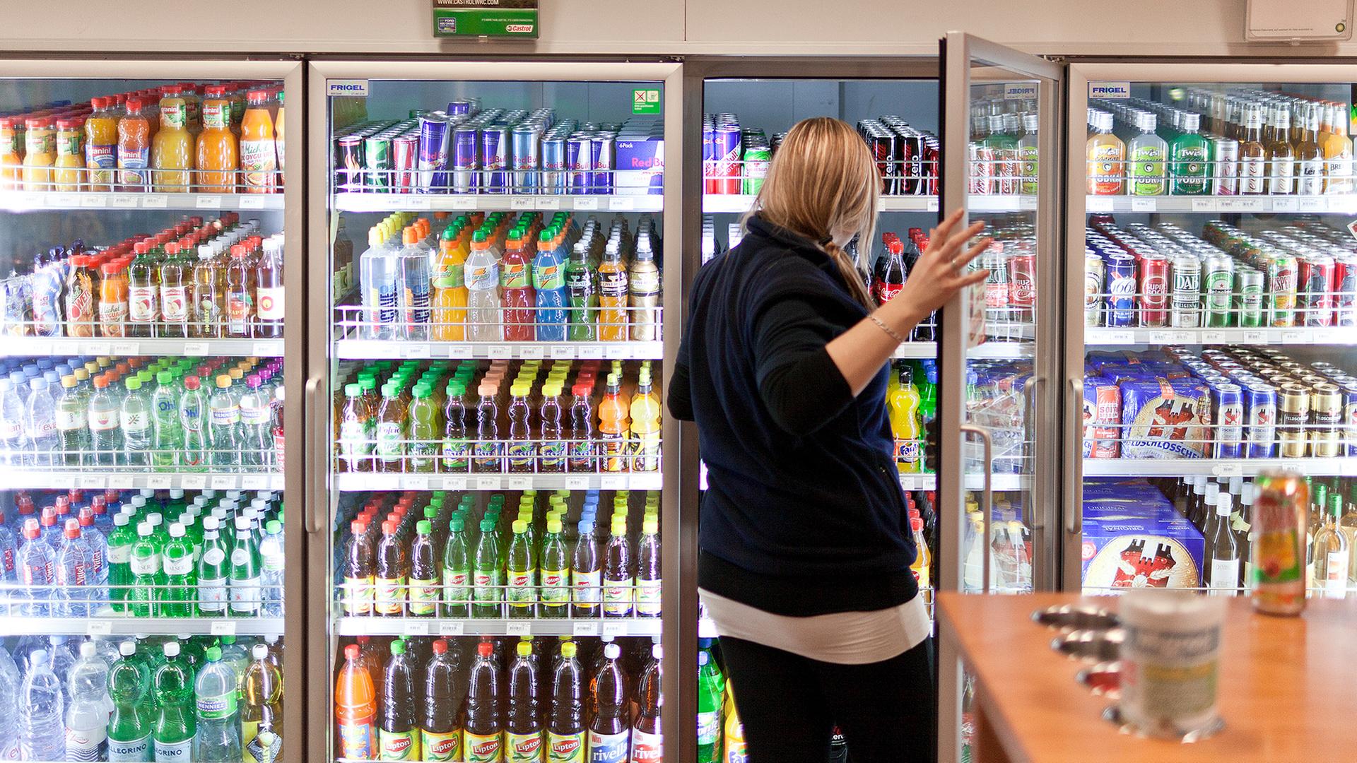 Eine Kundin bedient sich an einem Getränkeregal in einer Tankstelle. | picture alliance/KEYSTONE