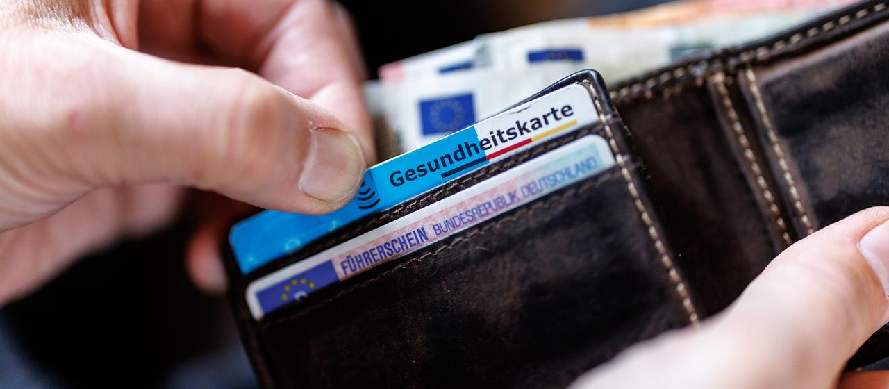 Ein Mann zieht eine Gesundheitskarte aus einer Geldbörse.